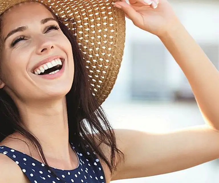 Stralende vrouw met hoed geniet van de zon met een gezonde, egale huid na een behandeling bij Apollo Beauty.